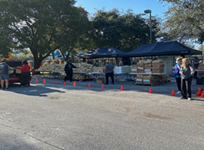 An outdoor scene at a city park, consisting of tents and resources to conduct a drive-thru food distribution.