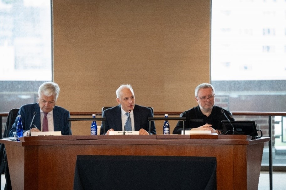 Three men sitting behind a desk with microphones.