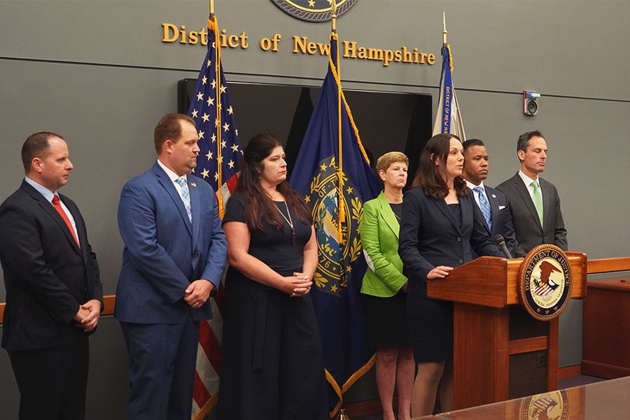 Assistant Administrator Kristi N. O'Malley of the DEA Diversion Control Division speaks at the podium with a Department of Justice seal. The background displays the seal of the district of New Hampshire.