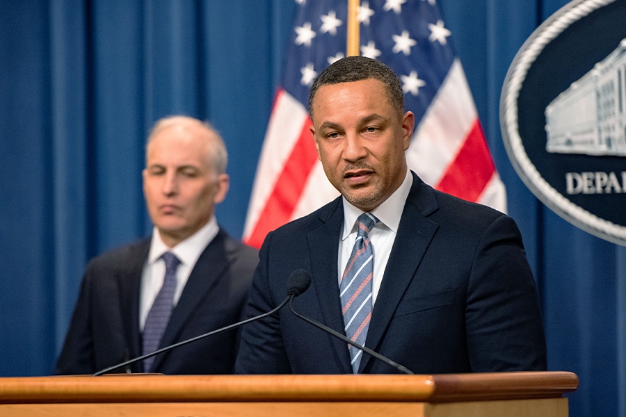 U.S. Attorney Breon Peace for the District of New York speaks at a podium with the Department of Justice seal in the background. To his left is Assistant Attorney General Matthew G. Olsen