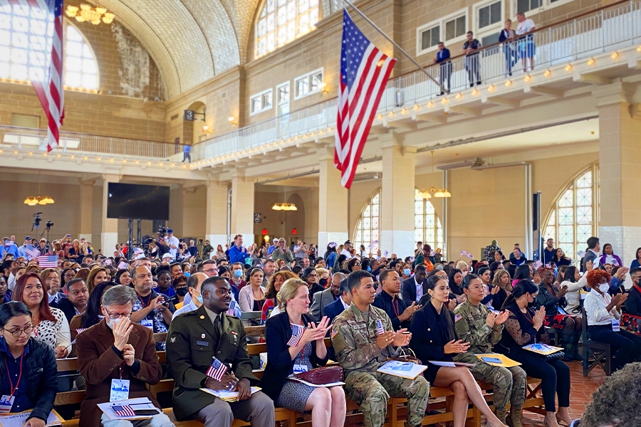 The audience in the Great Hall of Ellis Island in New York applauds in celebration.