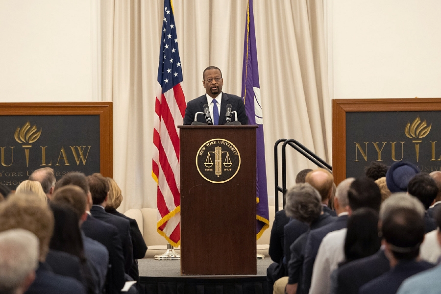 Dean Troy McKenzie of NYU’s School of Law speaks to an audience of officials and attorneys at a podium bearing the New York University seal.