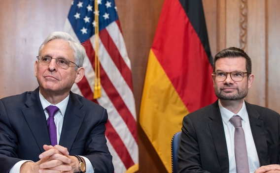 Attorney General Merrick B. Garland and the German Minister of Justice Dr. Marco Buschmann sit in front of the flag of the United States of America and the flag of Germany, respectively