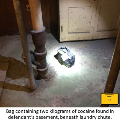 Image of zippered bag on basement floor. Text reads: Bag containing two kilograms of cocaine found in defendant's basement, beneath laundry chute.