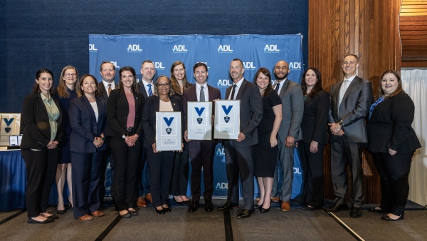 Group of attorneys, agents, and victim witness personnel pose in front of a Anti-Defamation League background accepting award 