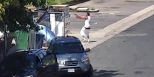 Surveillance photo of man in white shirt and white shorts holding arms out, firing a weapon down an alley